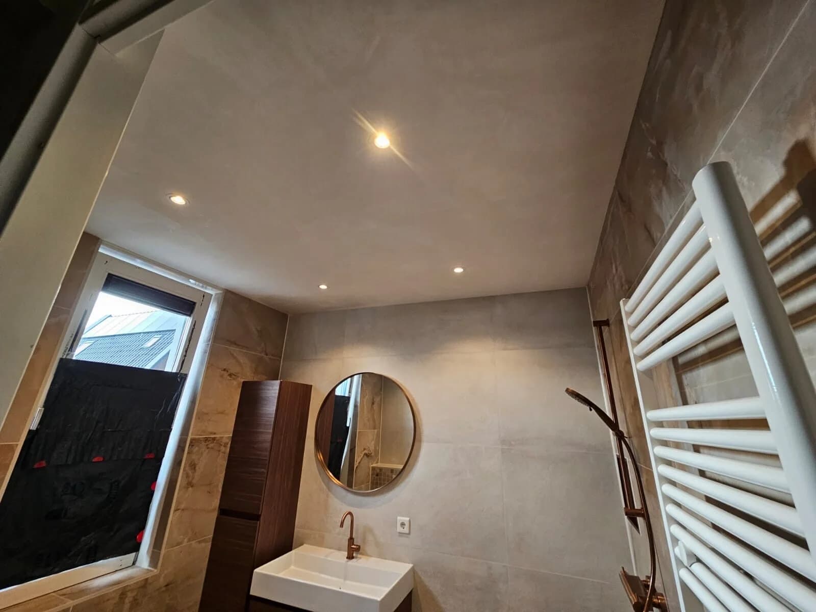 Badkamer met spanplafond en gouden ronde spiegel