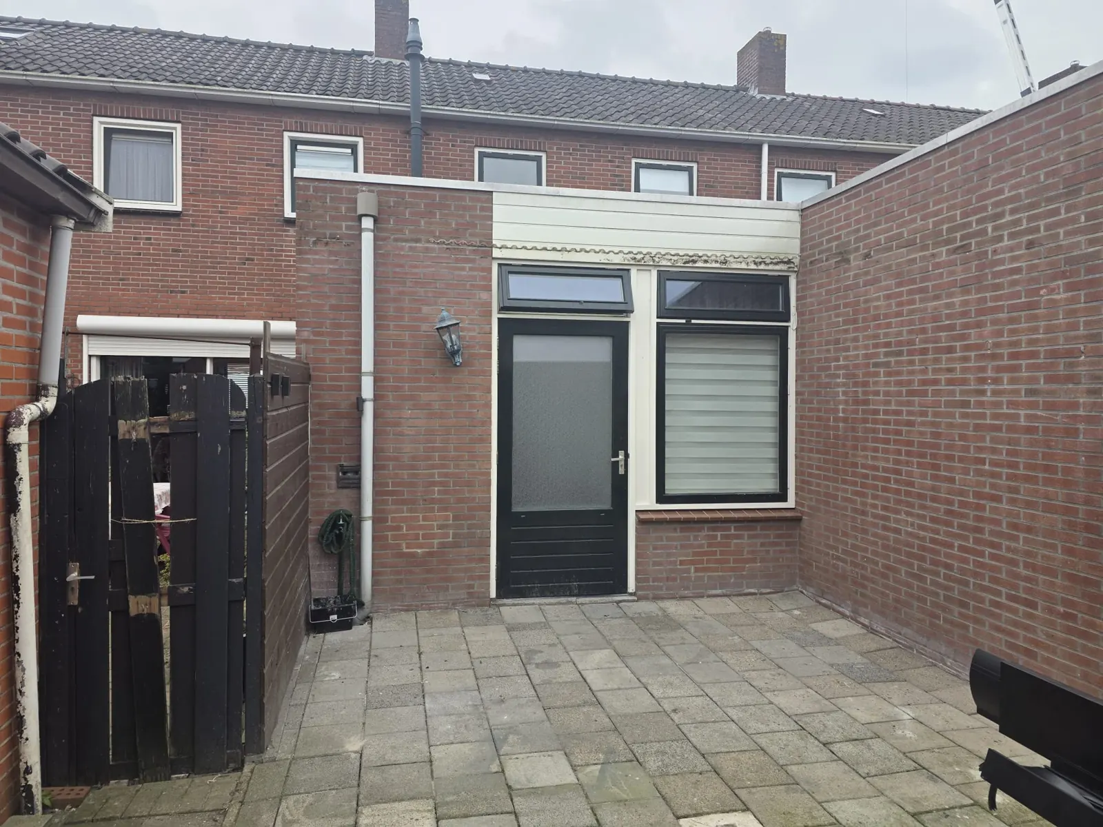 Open bestraat terras met bakstenen muren en achtergevel voor de overkapping in Alkmaar